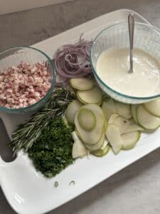 Tray with sliced vegetables, herbs, and sauce bowl.