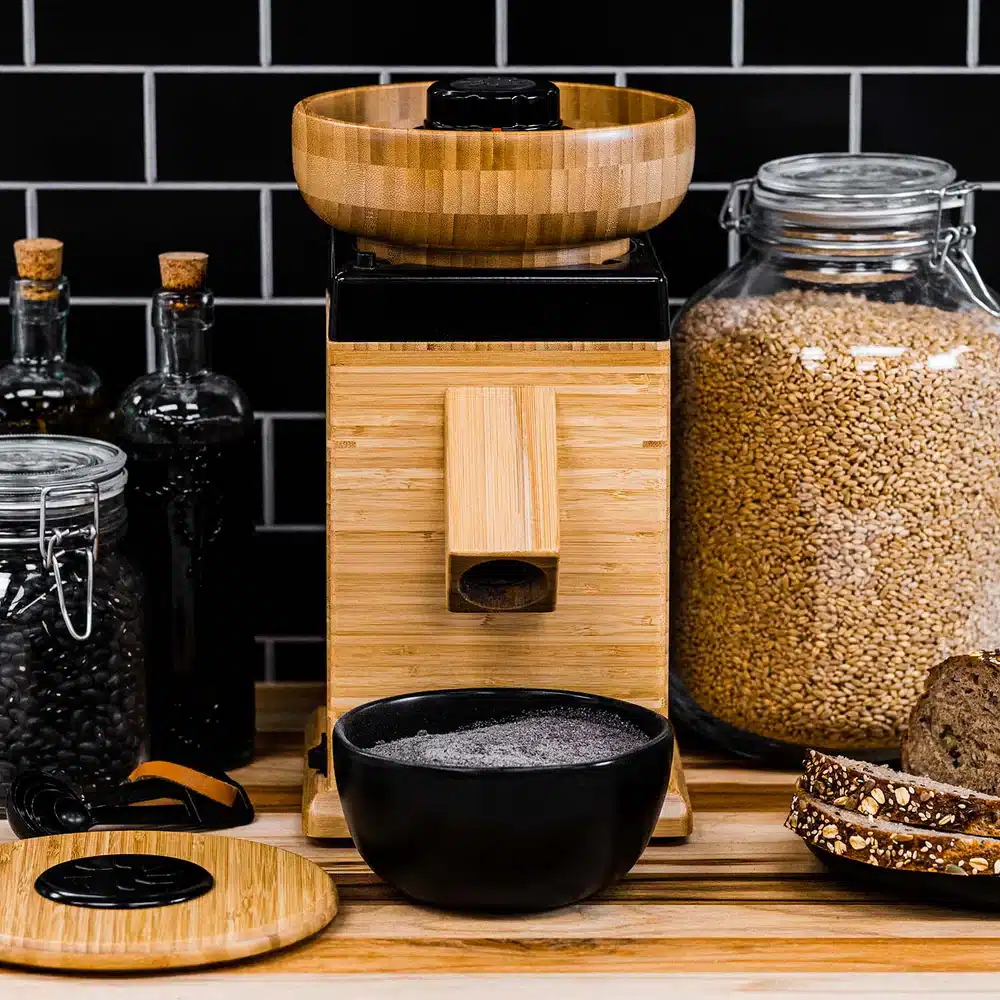 Wooden grain mill on kitchen counter with jars.