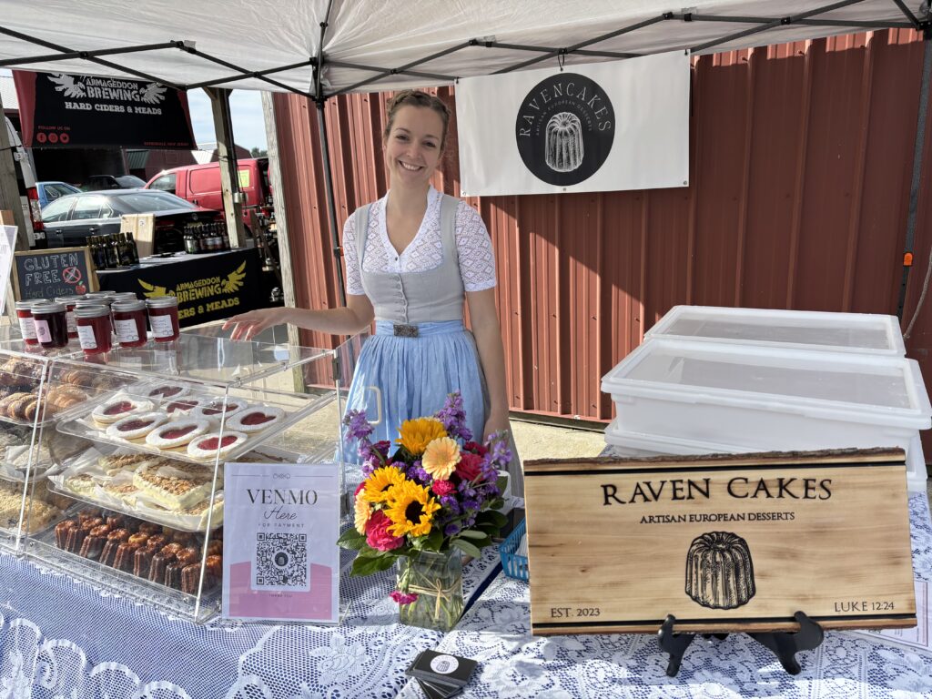 Raven Cakes stall with desserts and floral display.