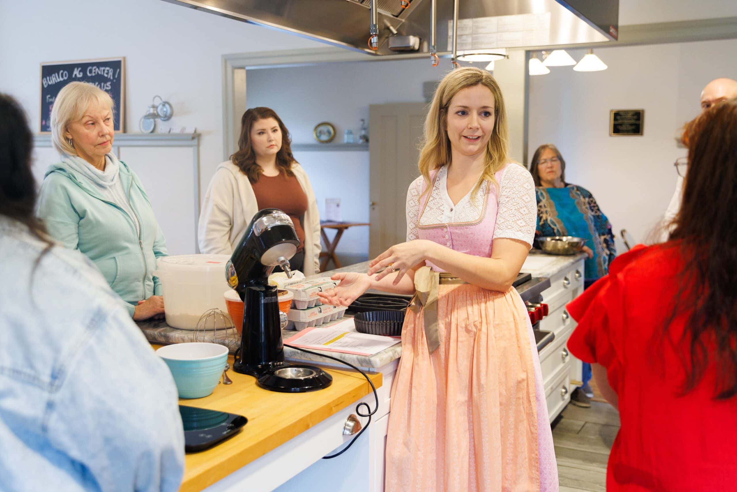 Woman leading cooking class with participants in kitchen.