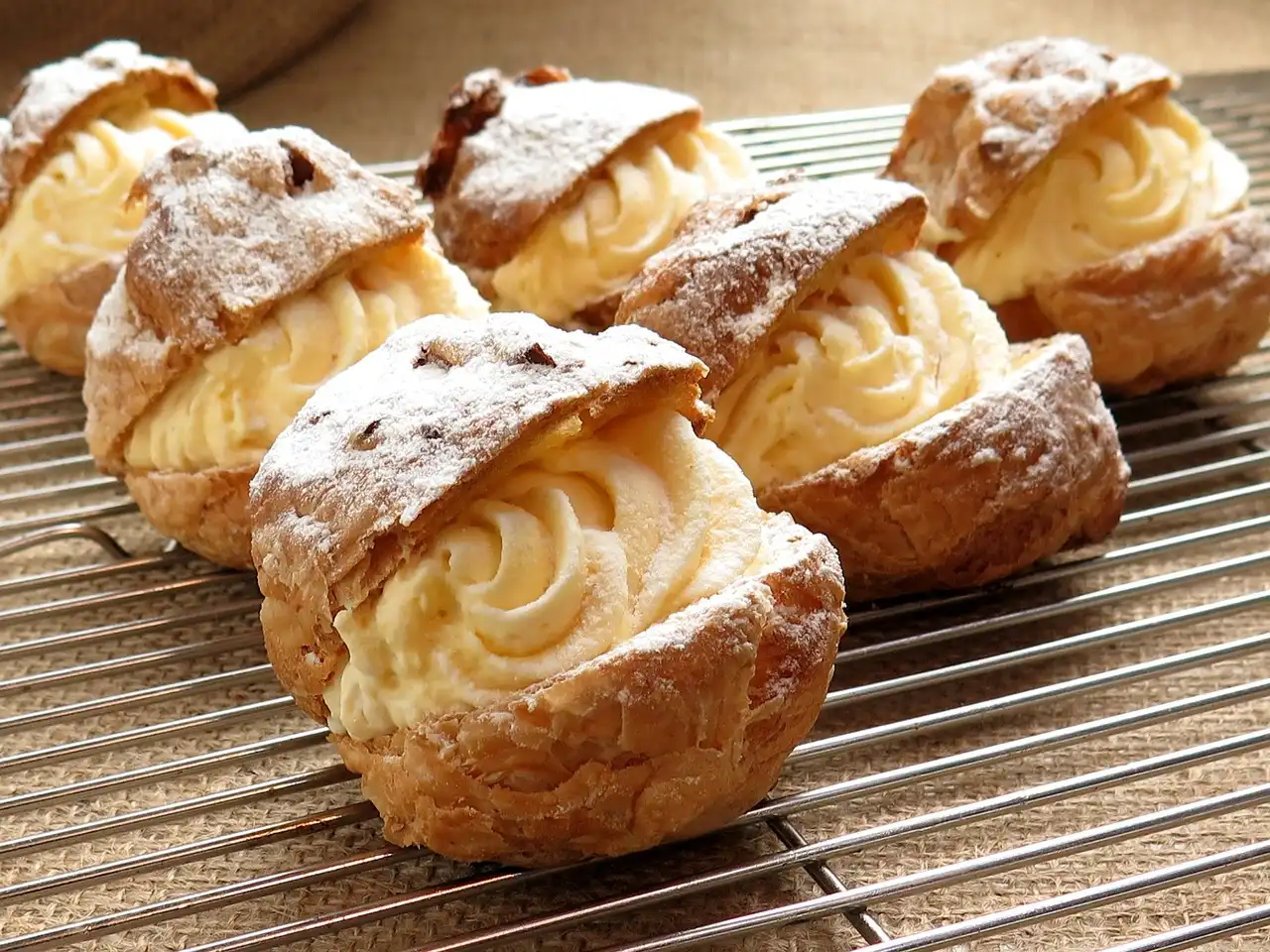 Cream puffs on cooling rack dusted with powdered sugar.