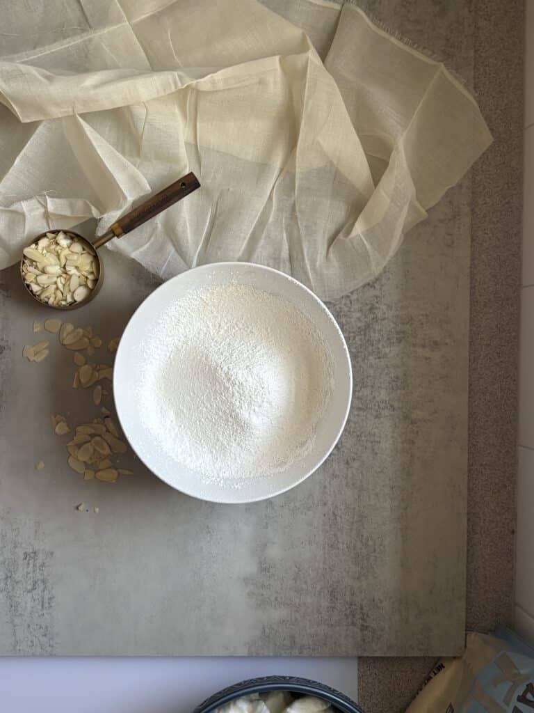 Bowl of flour and sliced almonds on cloth.