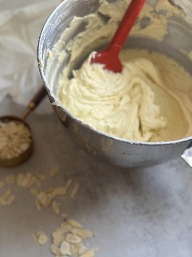 Bowl of cookie dough with red spatula and almonds.