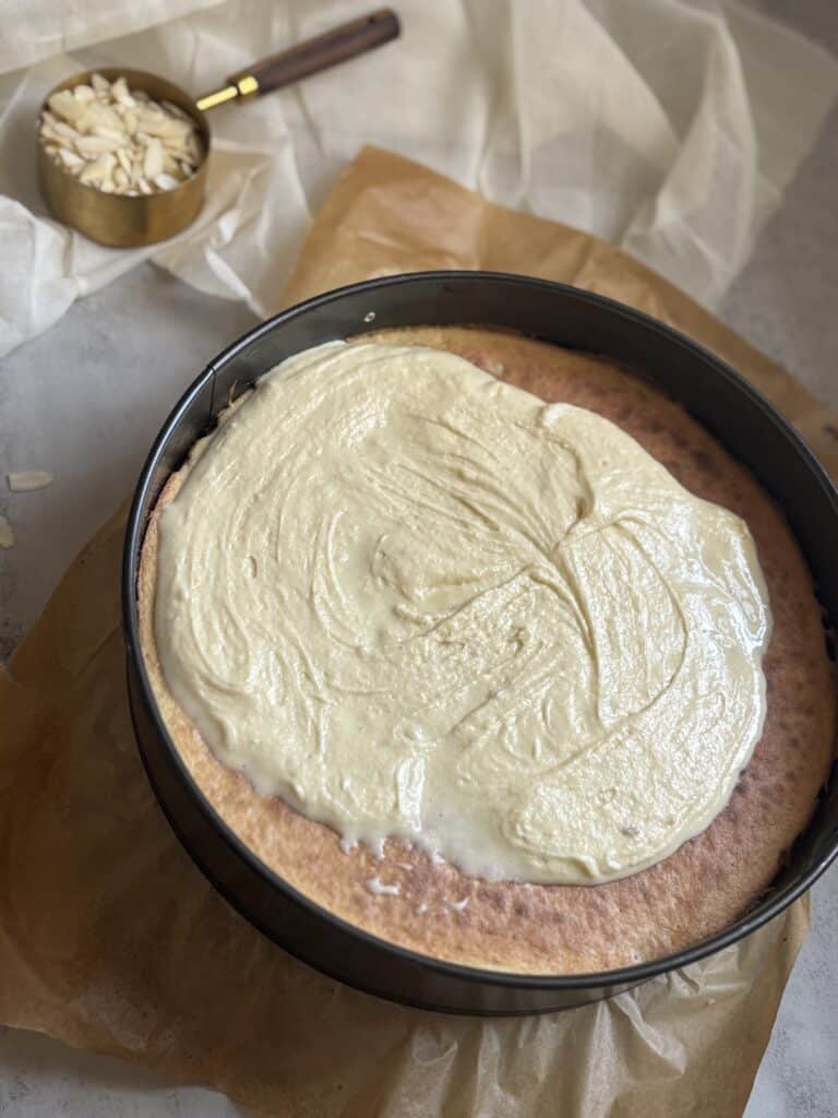 Cake with frosting in pan, almonds nearby.