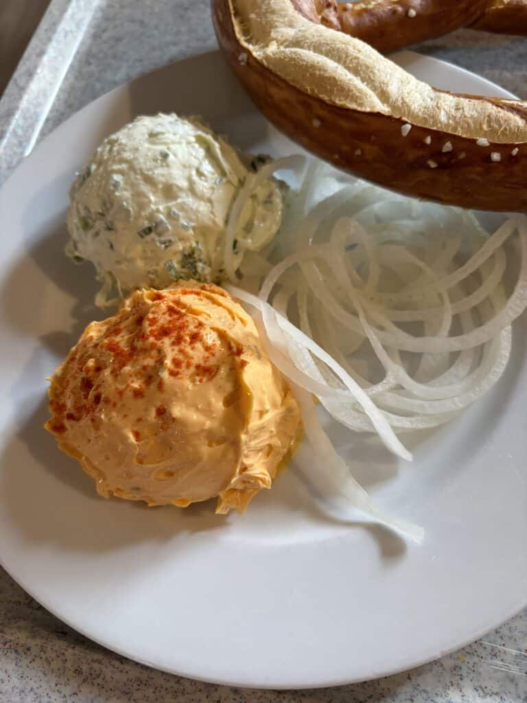 Plate with cheese spread, onions, and pretzel.