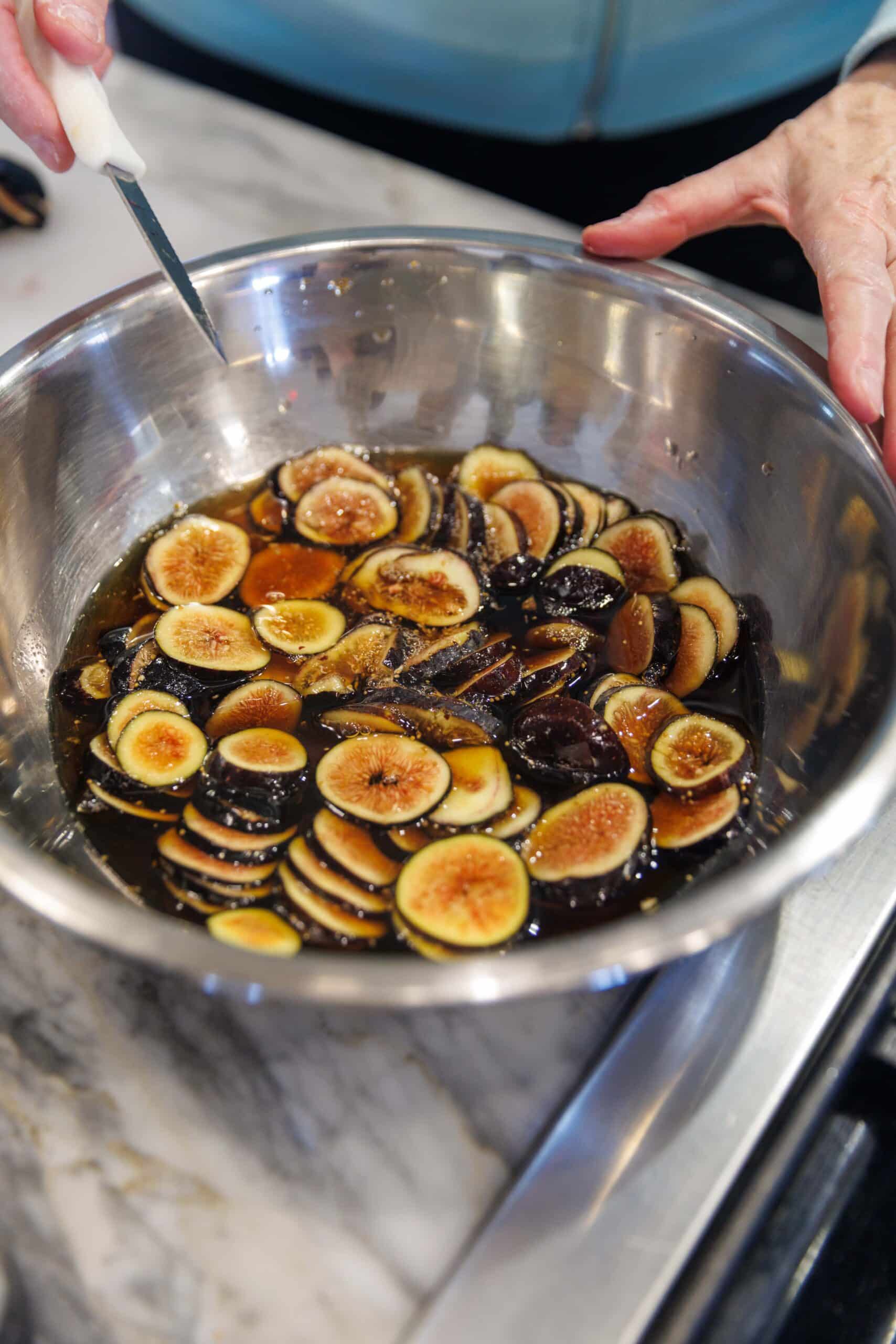 Sliced figs soaking in sherry wine in metal bowl.