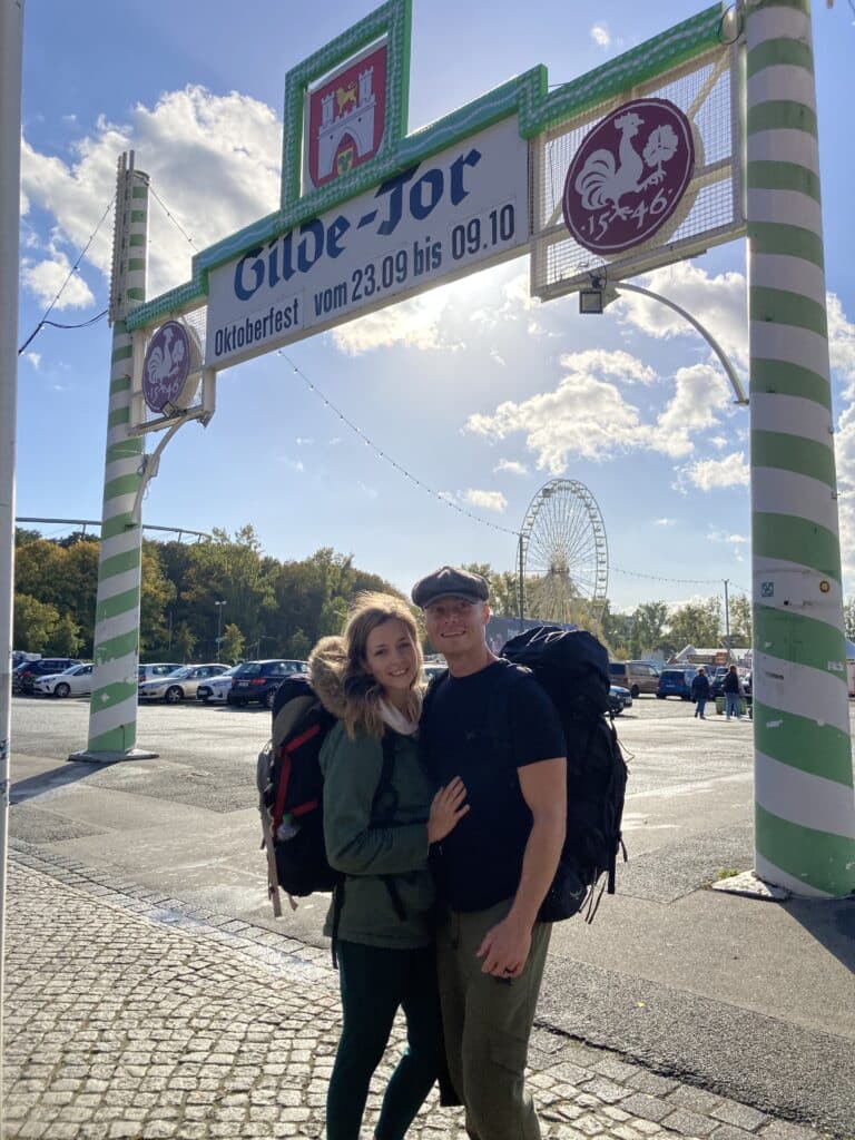 Couple under Oktoberfest entrance gate, sunny day.