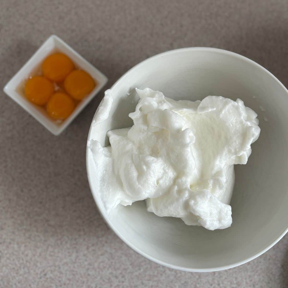 Egg yolks and whipped egg whites in separate bowls for carrot orange cake