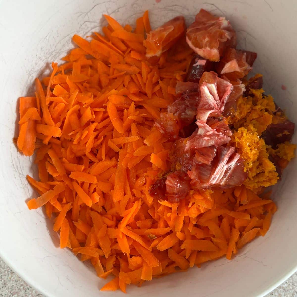 Grated carrots and chopped blood oranges in a bowl ready for carrot orange cake batter